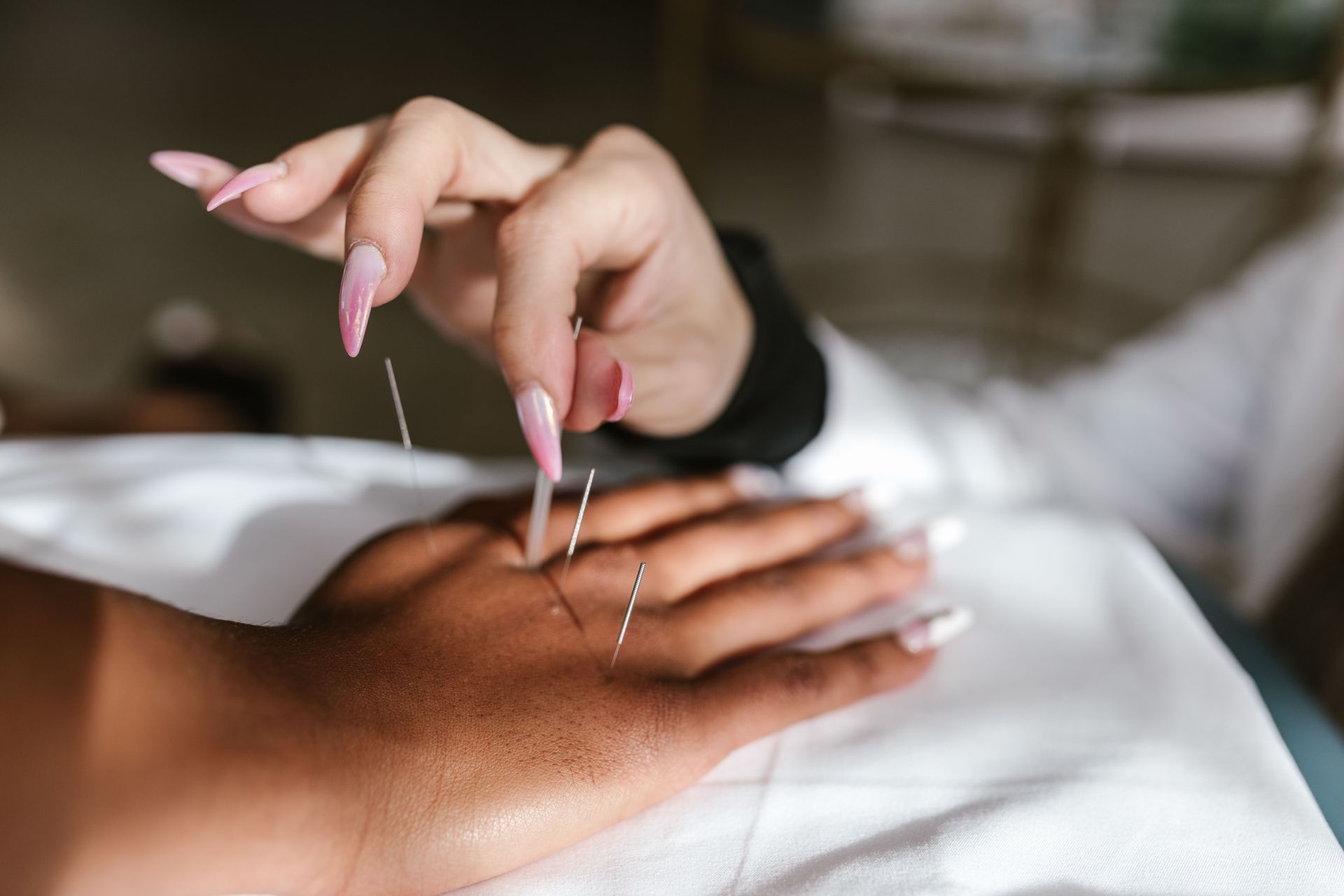 Une manucure applique de longs faux ongles roses en acrylique sur une main posée sur une serviette blanche.