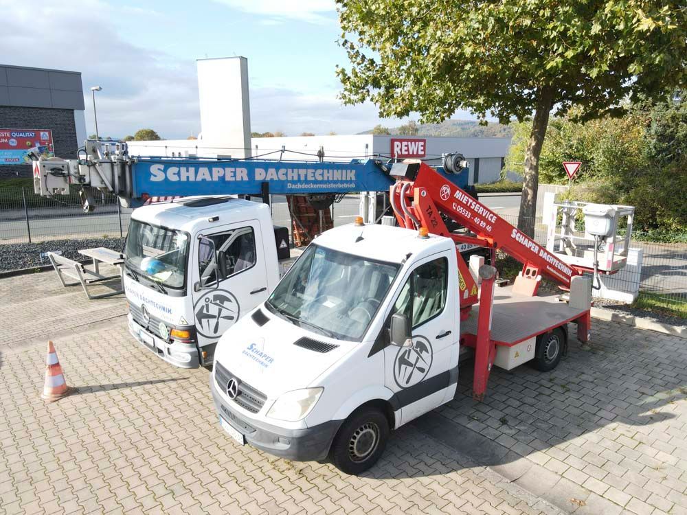 Ein orangefarbener Kran, der zu einem weißen Gebäude mit Fenstern emporragt; auf dem Kran ist „Schöttler“ aufgedruckt.