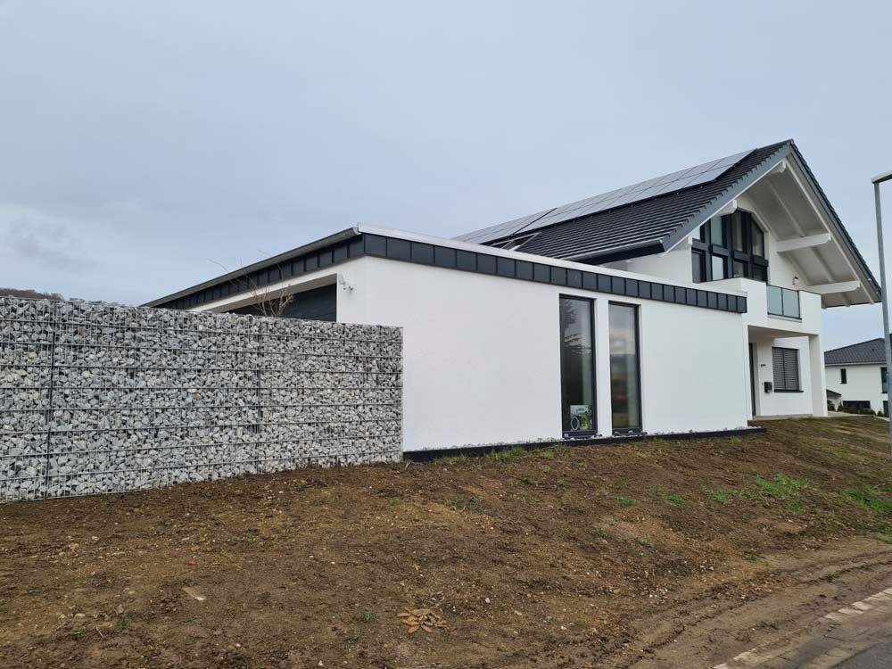 Modernes weißes Haus mit Gabionenwand an einem bewölkten Tag.