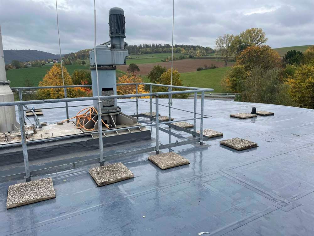 Dach mit Maschinen und Geländer. Quadratische Trittsteine ​​sind über die dunkle Fläche verstreut, mit Blick auf eine ländliche Landschaft.