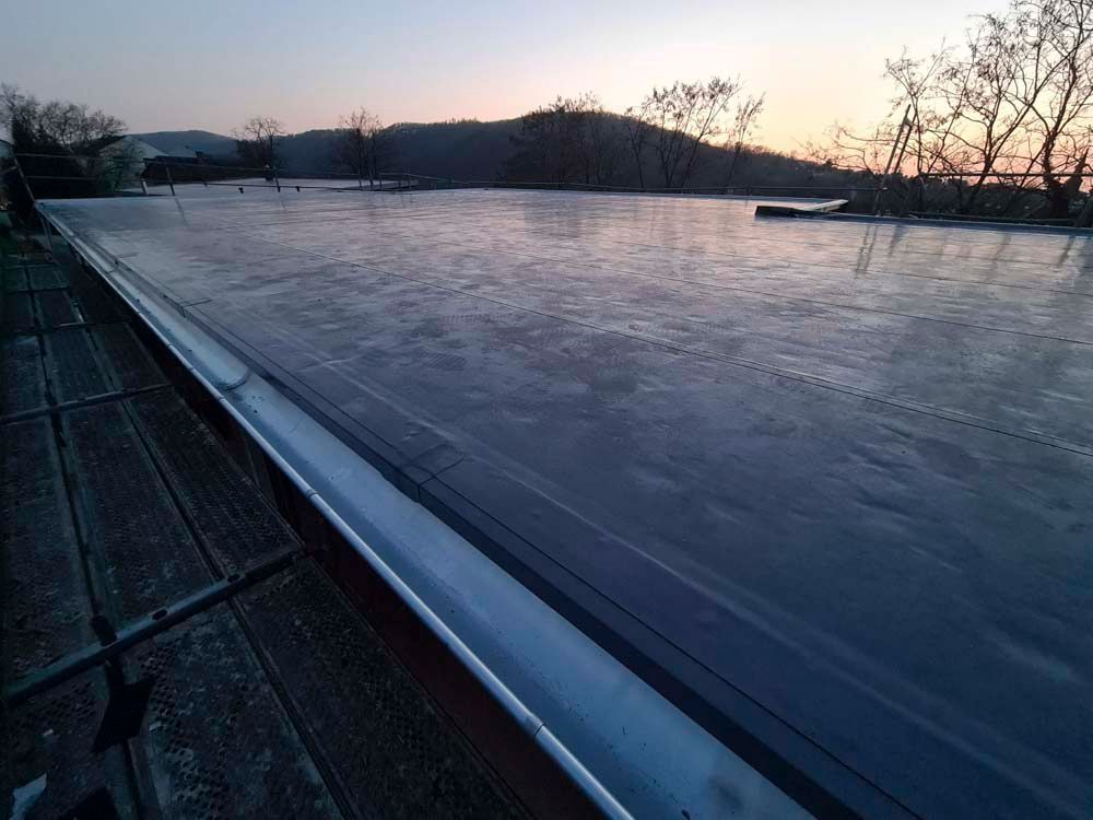 Ein zugefrorener See in der Abenddämmerung, im Hintergrund Bäume und ein Hügel. Der Himmel leuchtet in Orange- und Rosatönen.