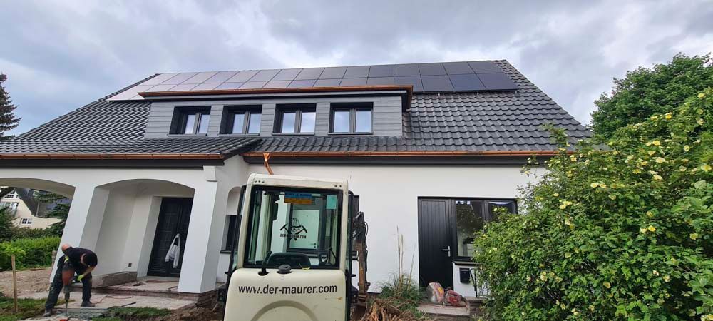 Weißes Haus mit dunklem Dach und Zierelementen unter bewölktem Himmel, aus einem leicht nach unten gerichteten Winkel gesehen.