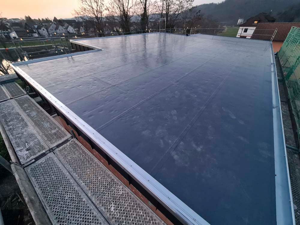 Ein Innenhof mit gepflasterter Terrasse, Kiesbodenbelag, Topfpflanzen und Oberlicht. Gebäude mit weißen und braunen Außenfassaden umgeben den Raum.