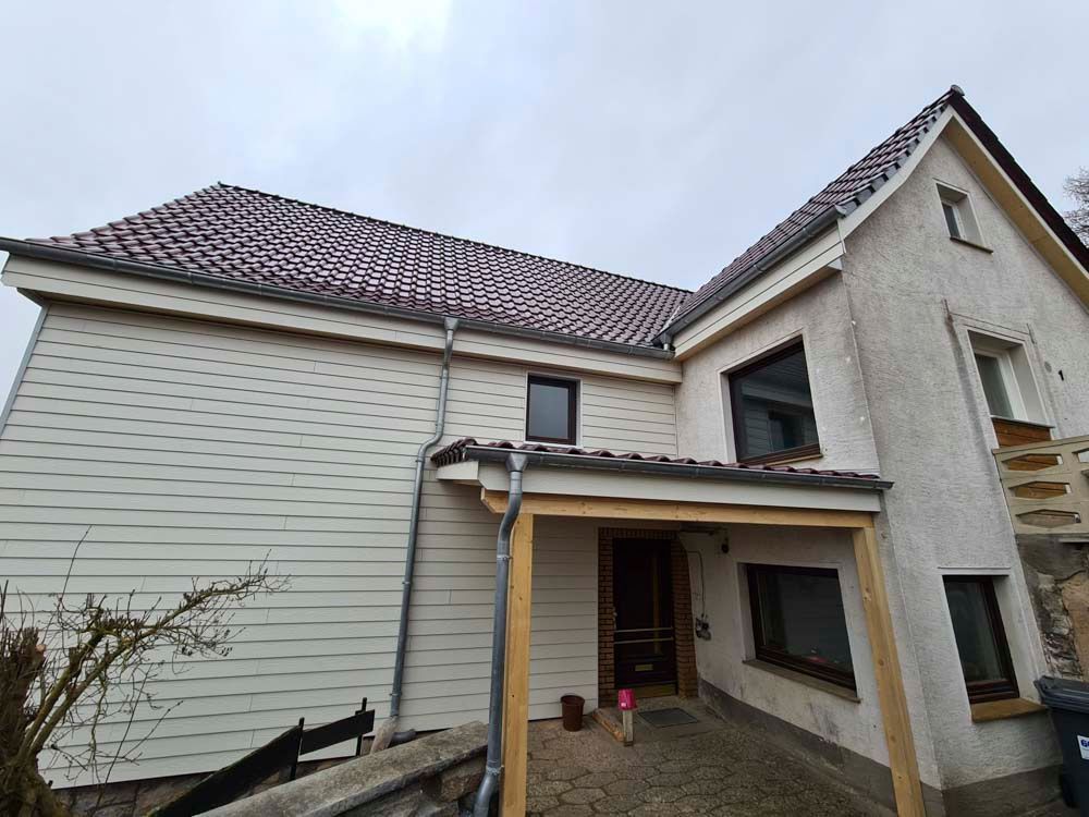 Beiges Haus mit Ziegeldach und heller Fassade unter bewölktem Himmel.