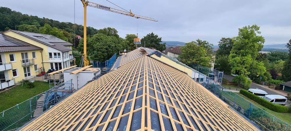 Dachstuhl eines im Bau befindlichen Gebäudes, im Hintergrund ein gelber Kran und weitere Gebäude.