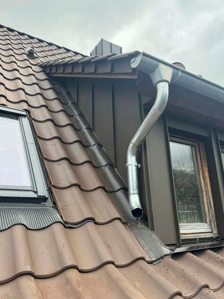 Braunes Ziegeldach mit Metallrinne und Fallrohr.