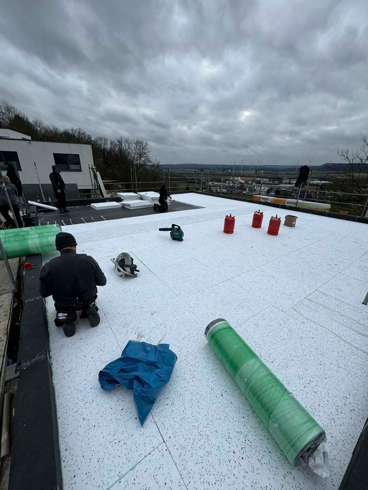 Bauarbeiter verlegen an einem bewölkten Tag weiße Dämmung auf einem Flachdach.