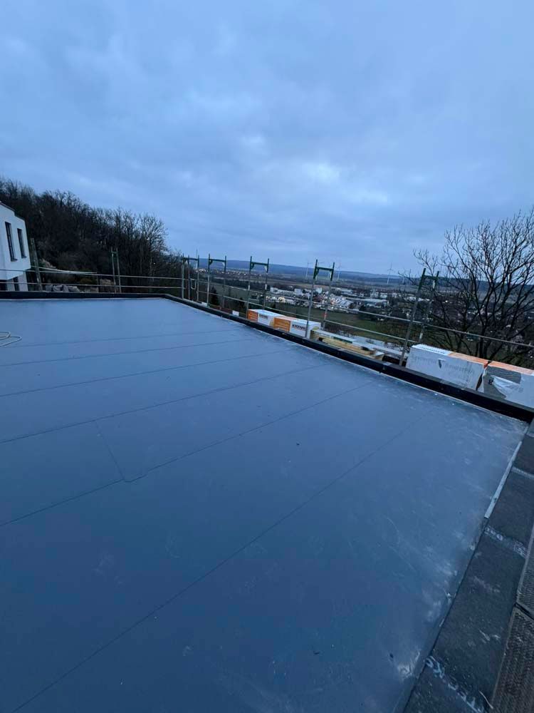 Flaches, dunkles Dach mit einer Stadtkulisse im Hintergrund unter bewölktem Himmel.