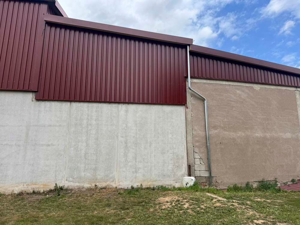 Burgunderrote Wellblechverkleidung an einem Gebäude mit einer Beton- und Stuckwand, Dachrinne rechts.