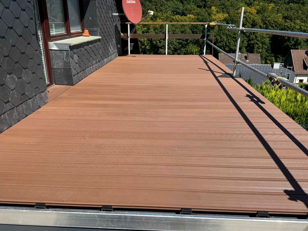 Holzterrasse mit Geländer, angrenzend an ein Haus mit dunkelgrauer Fassadenverkleidung.