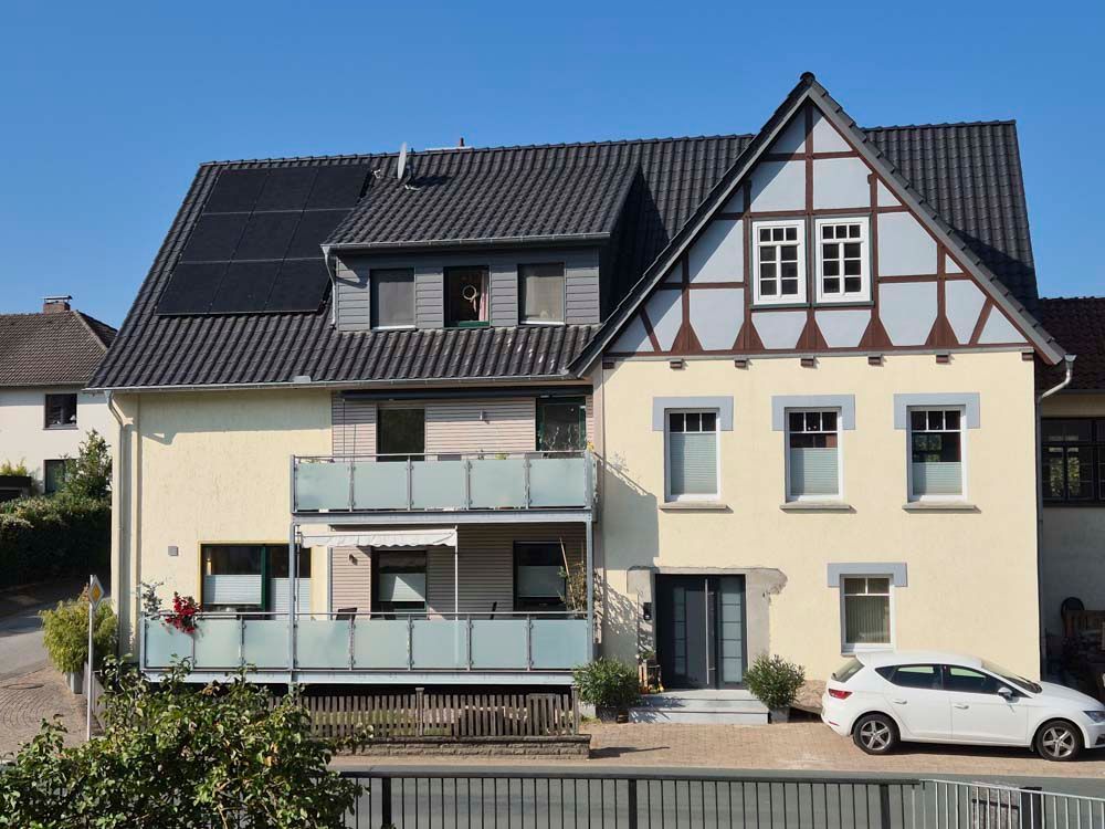Zweistöckiges Haus mit Solarpaneelen, Balkon und einem davor geparkten weißen Auto.