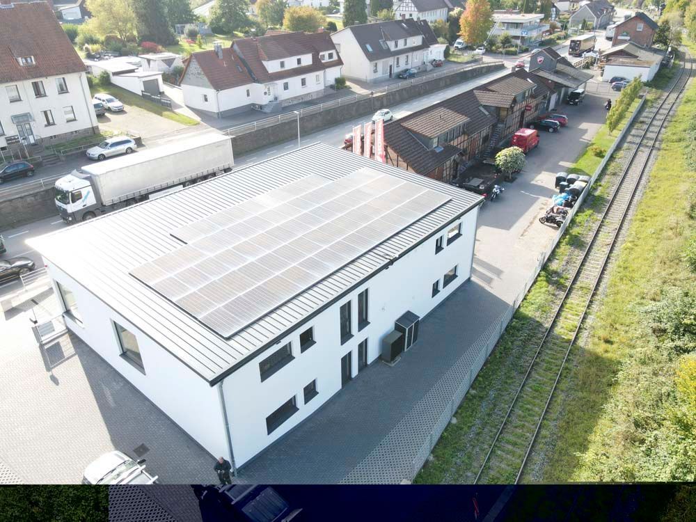 Gebäude mit Solarpaneelen auf dem Dach, in der Nähe von Bahngleisen und anderen Gebäuden.