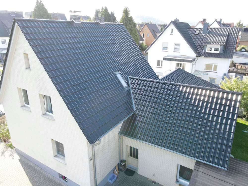 Weißes Haus mit dunkelgrauem Ziegeldach, Fenstern und einer kleinen Eingangstür.