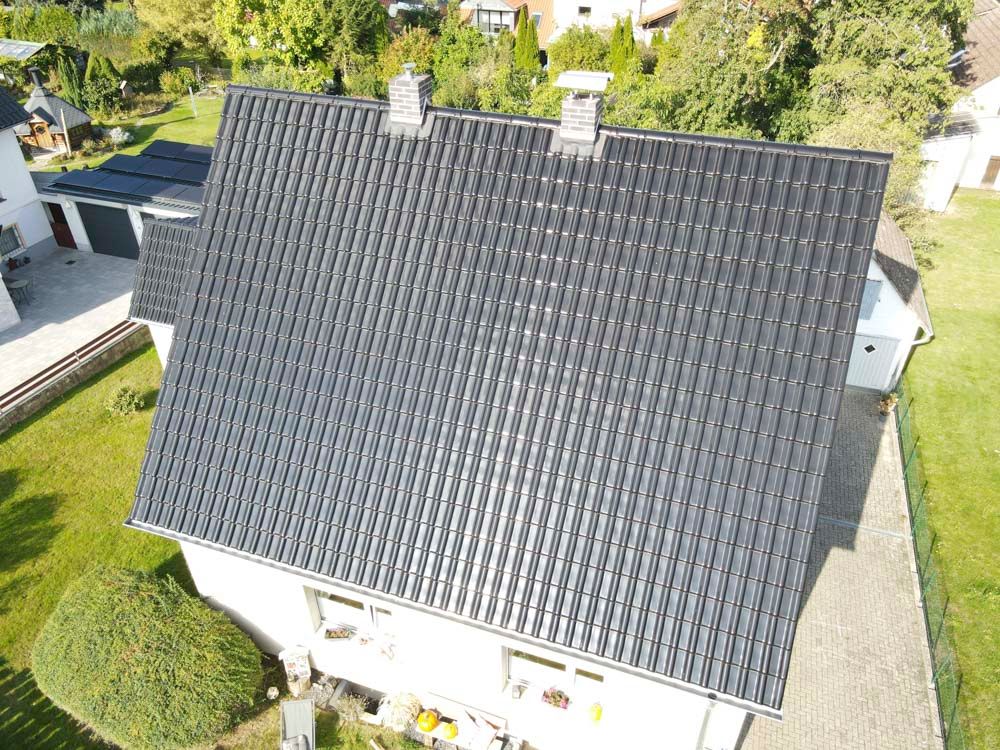 Draufsicht auf ein Haus mit dunklem Ziegeldach, zwei Schornsteinen und grünem Rasen.