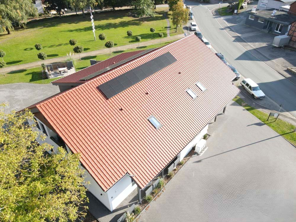 Luftaufnahme eines Gebäudes mit rotem Ziegeldach, Solarpaneelen und Oberlichtern neben einer Straße und einer Rasenfläche.