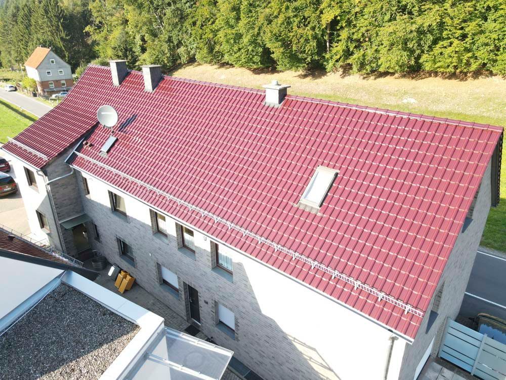 Gebäude mit rotem Ziegeldach; umgeben von Bäumen und einer Straße.