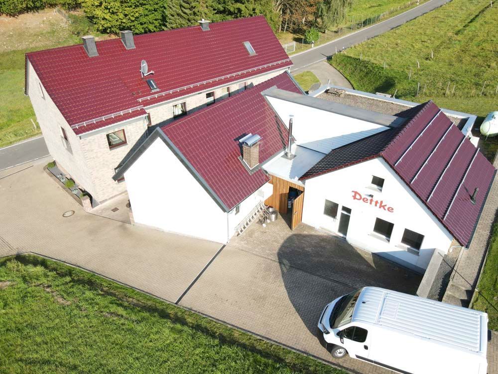 Ein weißes Gebäude mit bordeauxrotem Dach und dem Schriftzug „Doitko“ an der Fassade, daneben ein Gebäude mit rotem Dach, davor ein Lieferwagen geparkt.