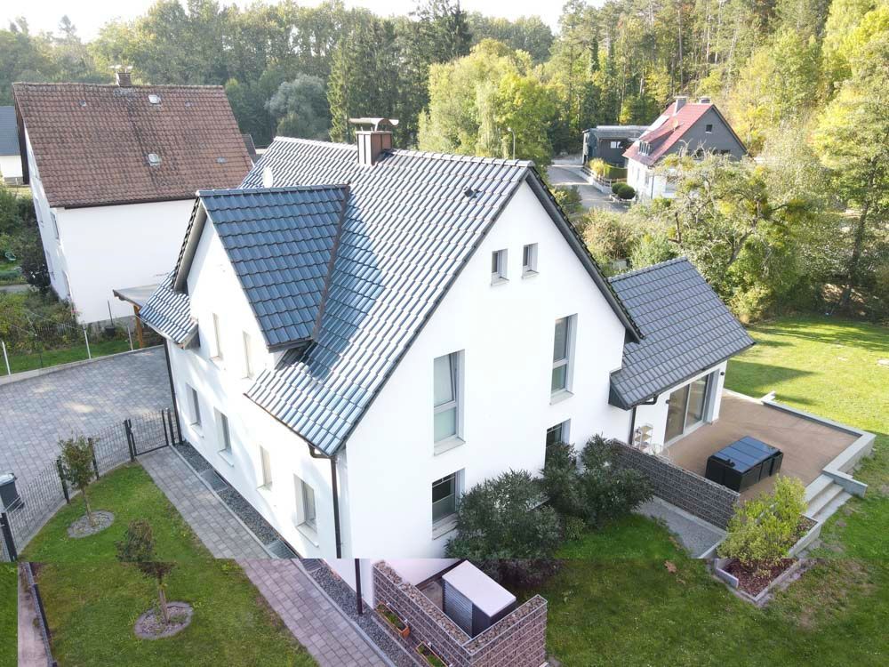 Weißes Haus mit grauem Dach, umgeben von grünem Gras und Bäumen.