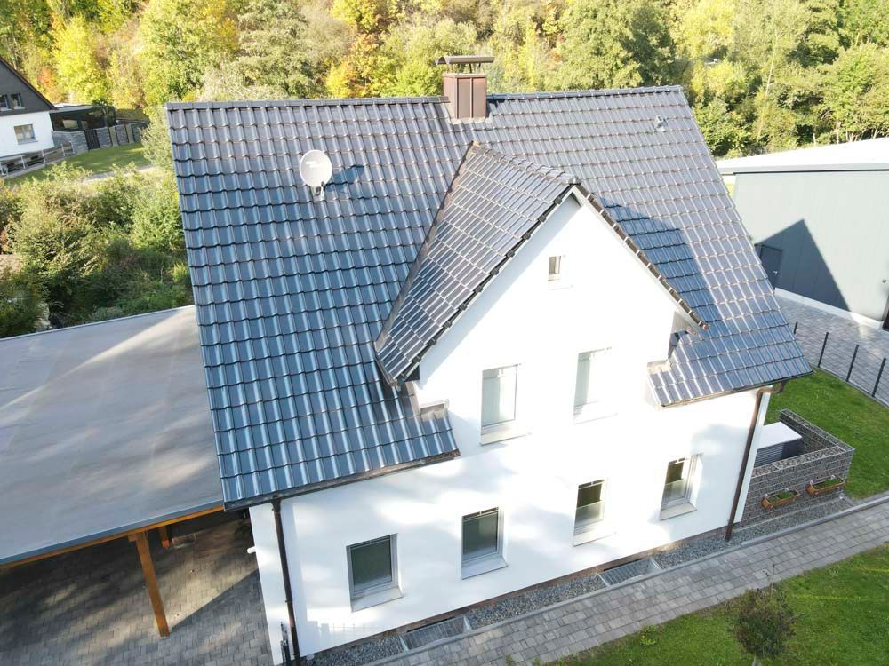 Weißes Haus mit dunkelgrauem Dach, Carport und umliegendem Grün.
