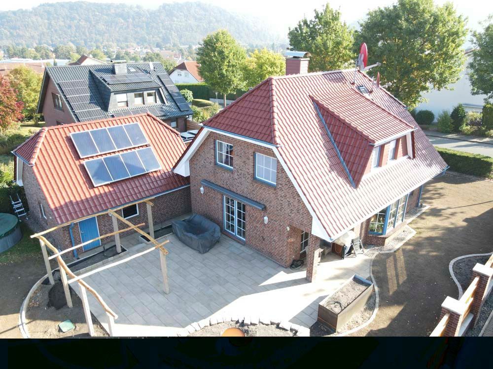 Haus mit rotem Ziegeldach, Backsteinfassade und Solaranlage. Terrasse mit Pflastersteinen, Holzkonstruktion und angelegtem Garten.