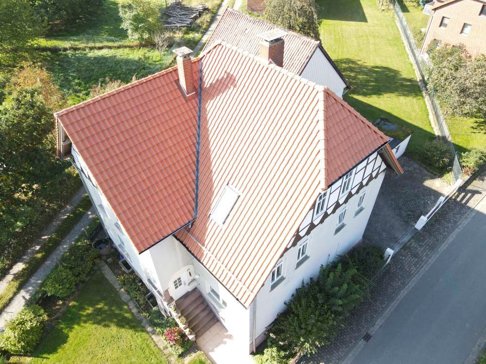 Weißes Haus mit schwarzem Dach, Schornstein und Fenstern. Vor dem Haus parkt ein weißer Lieferwagen.