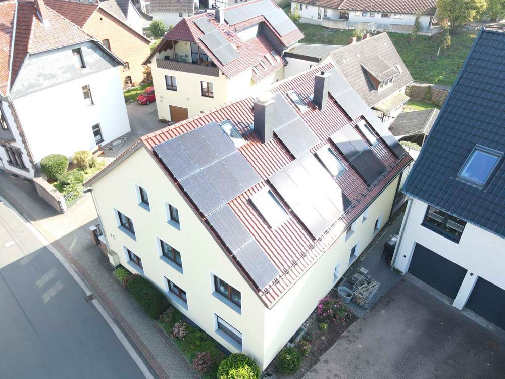 Solarpaneele auf einem zweistöckigen beigen Haus mit rotem Dach, neben anderen Häusern.