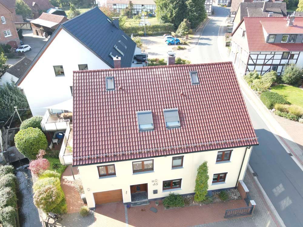 Draufsicht auf ein zweistöckiges beigefarbenes Haus mit rotem Ziegeldach, umgeben von anderen Gebäuden und einer Straße.