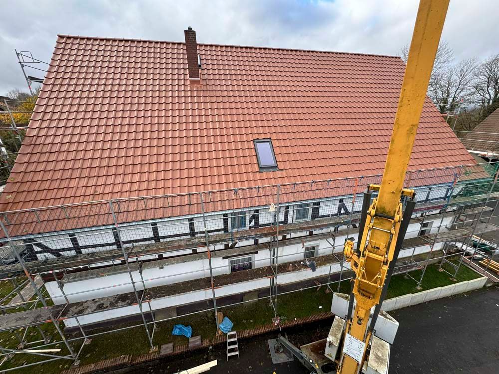 Ein Fachwerkhaus mit rotem Ziegeldach und Gerüst. Ein Kran ragt ins Bild. Bewölkter Himmel.