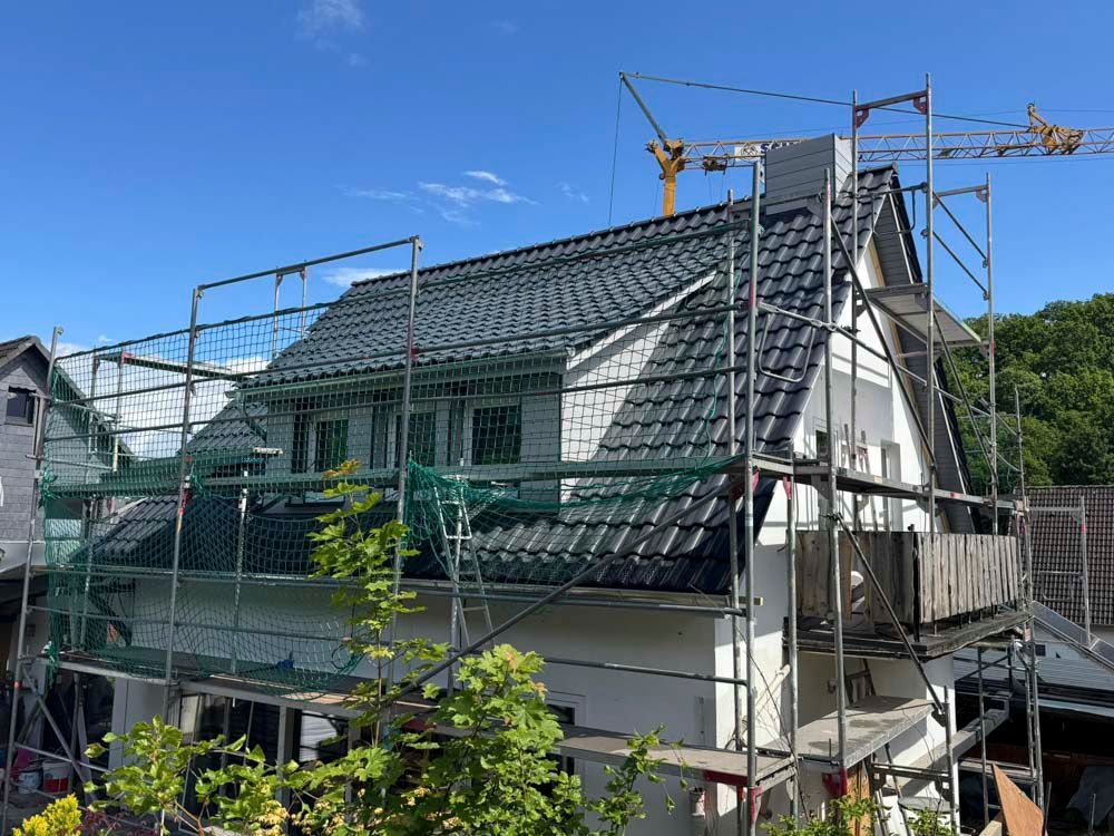 Haus mit dunkelgrauem Dach im Bau; Gerüst und Kran sind zu sehen.