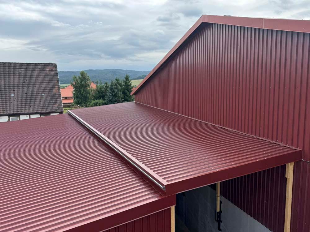 Rotes Wellblechdach und -fassade an einem Gebäude mit Carport vor bewölktem Himmel.