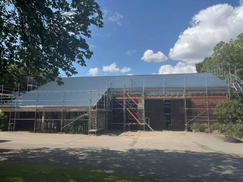Ein im Bau befindliches Gebäude mit Gerüst und Plane auf dem Dach, draußen unter blauem Himmel.