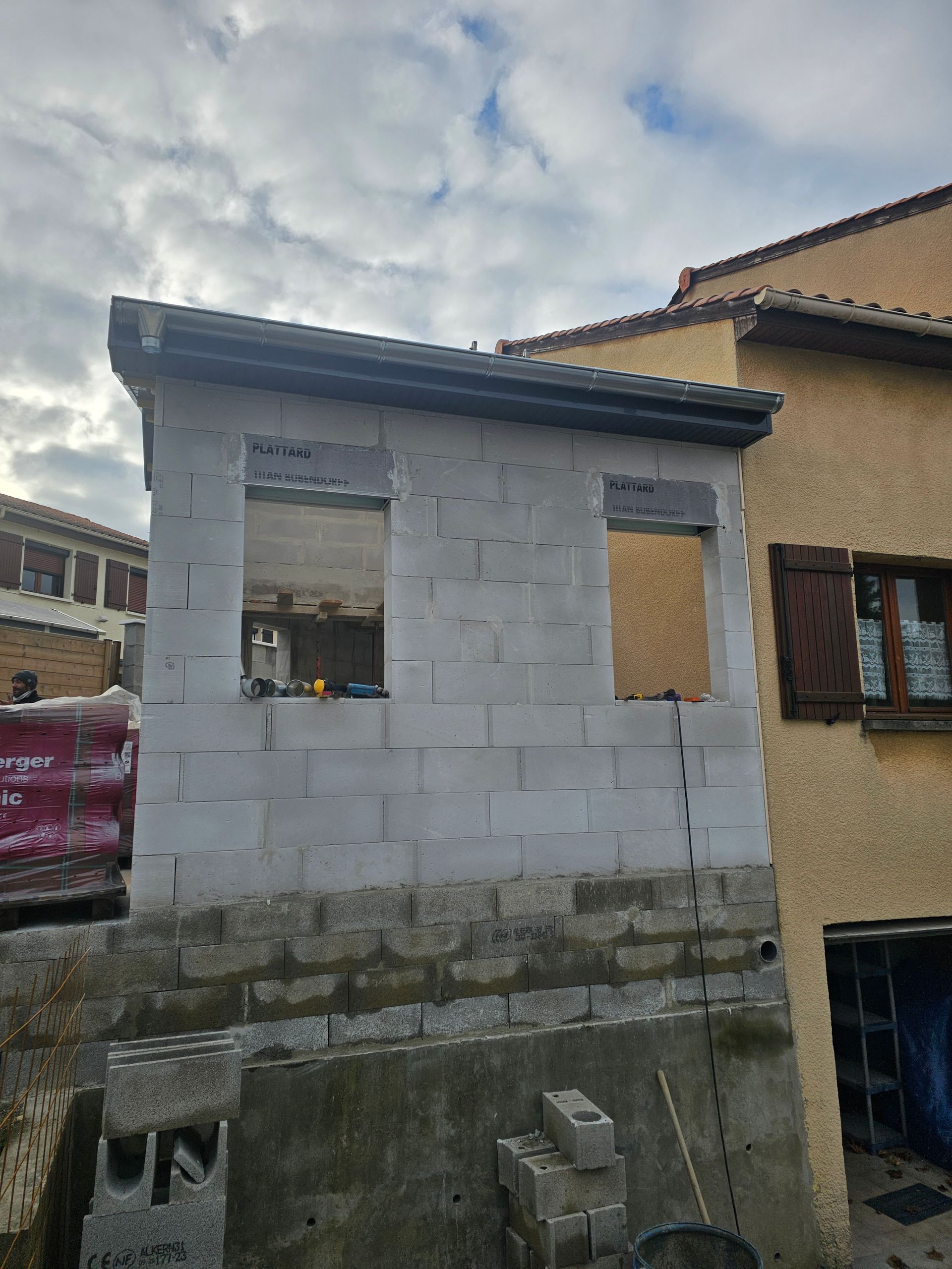 Une extension de maison inachevée, construite en blocs de béton cellulaire blanc, comportant deux ouvertures encadrées pour des fenêtres.