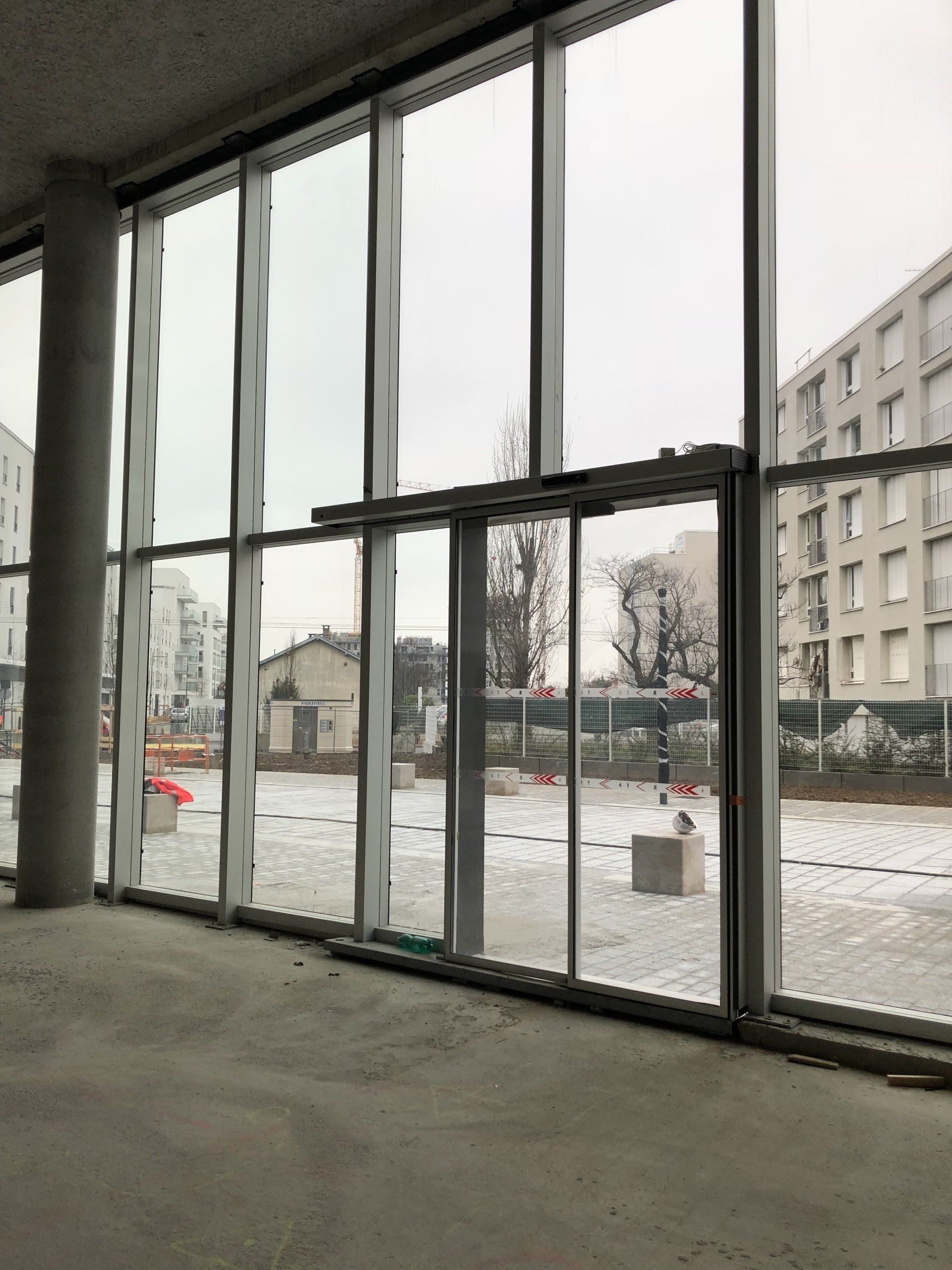 Grande baie vitrée avec porte coulissante automatique, donnant sur un espace extérieur enneigé avec des bâtiments.