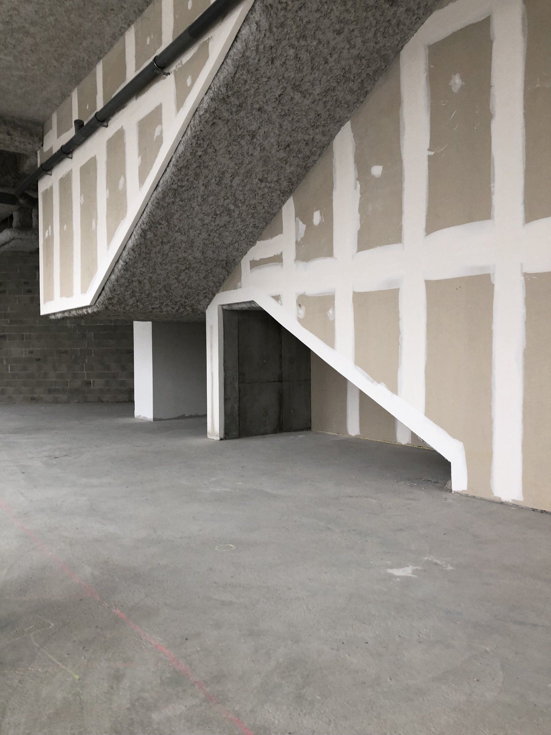 Un espace de construction intérieur inachevé présentant une structure d'escalier en béton avec des cloisons sèches et des joints apparents.
