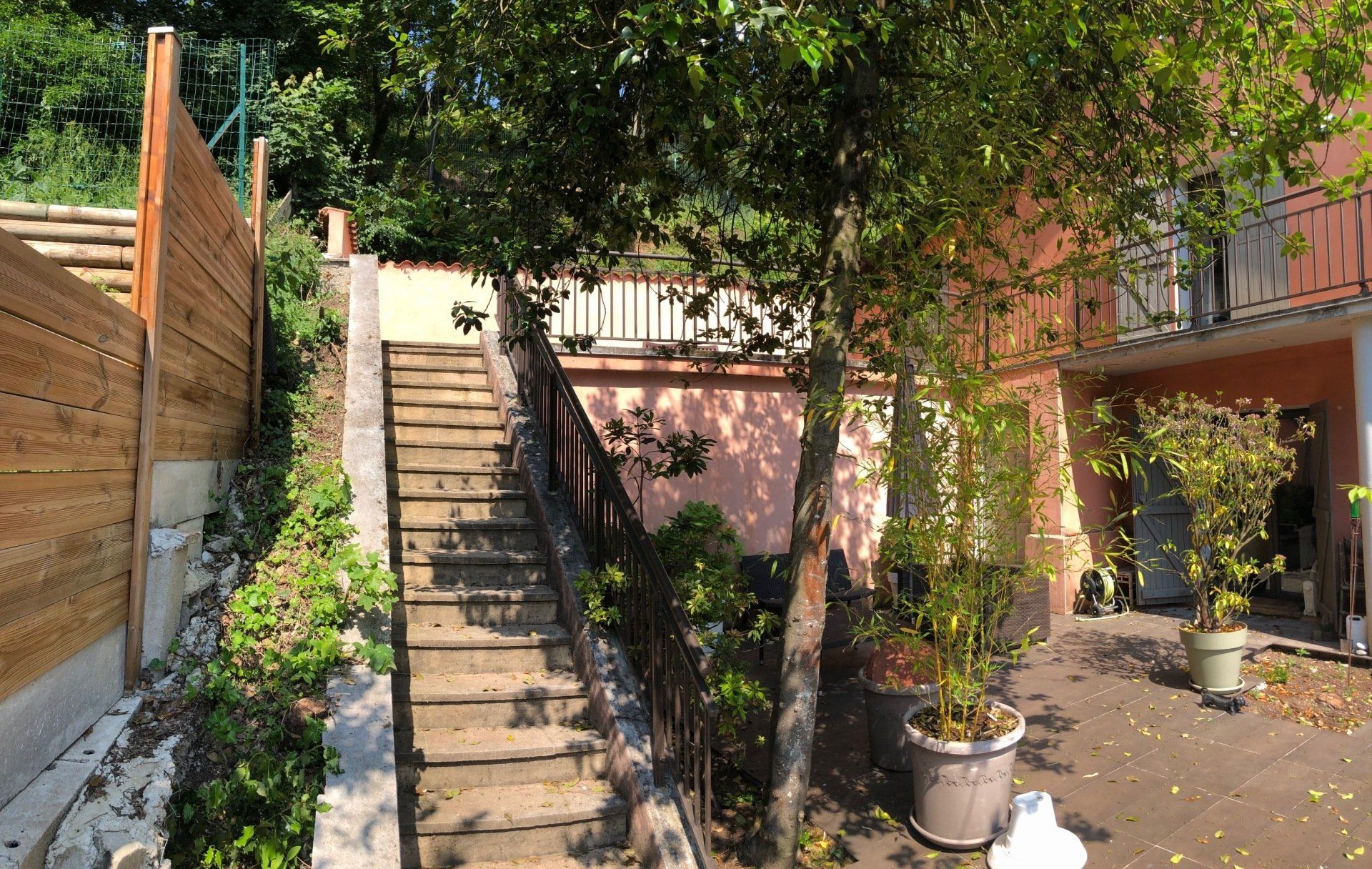 Un escalier aux marches en bois menant à un palier jouxtant un bâtiment couleur pêche orné de plantes en pot.