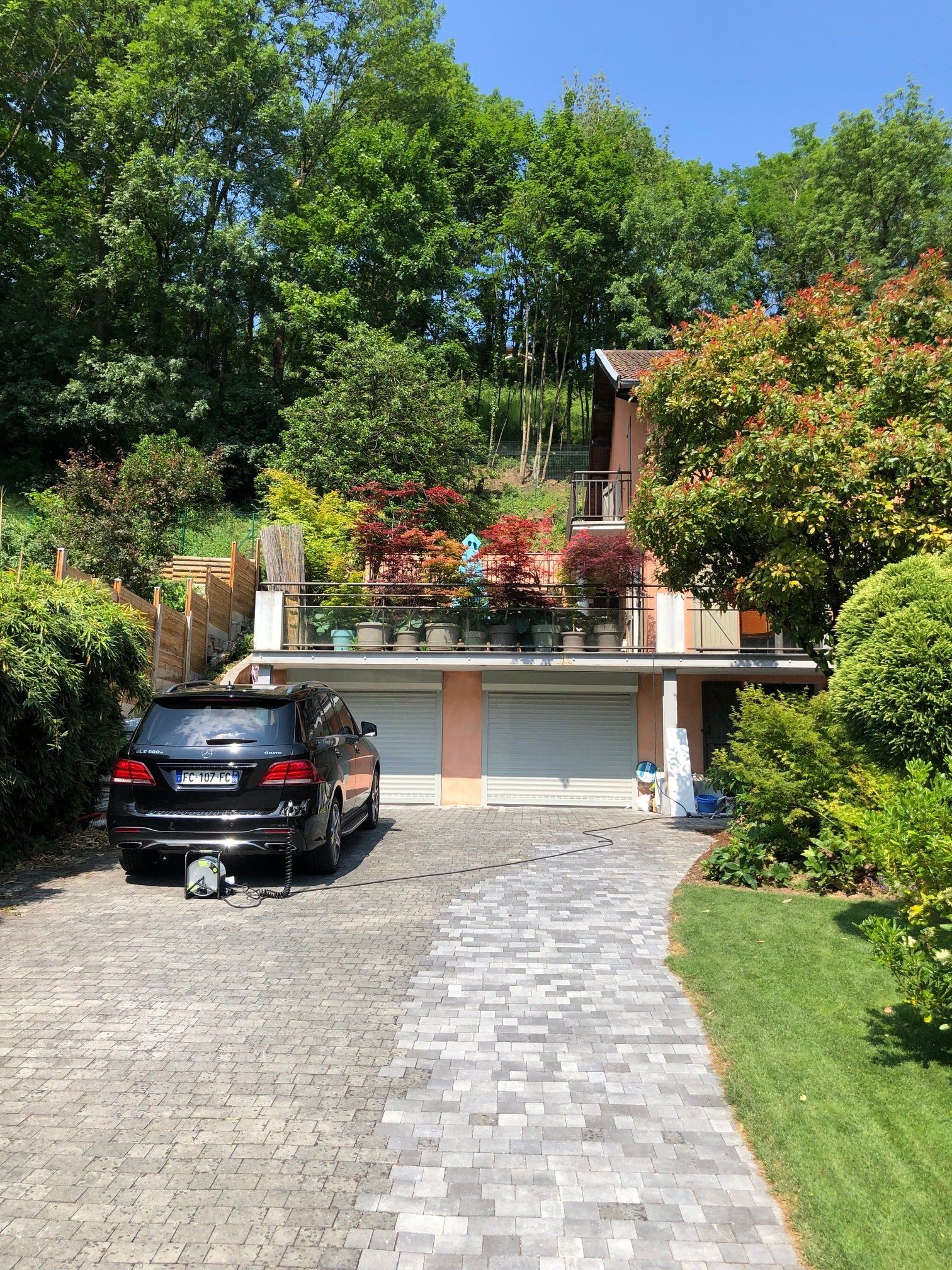 Un SUV noir garé sur une allée pavée devant une maison à deux étages avec un balcon rempli de plantes en pot.