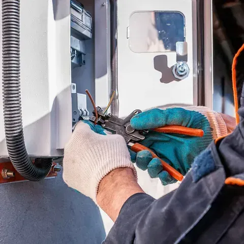 Un hombre está trabajando en una caja eléctrica con alicates.