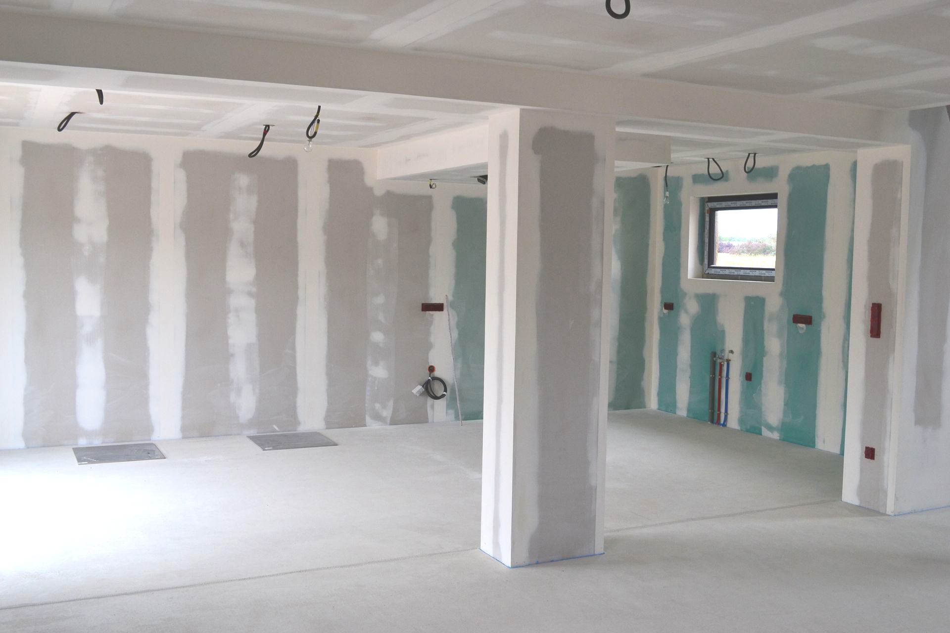Intérieur d'une pièce en construction, murs et plafond en plaques de plâtre. Des fils électriques pendent et certains murs sont apprêtés.