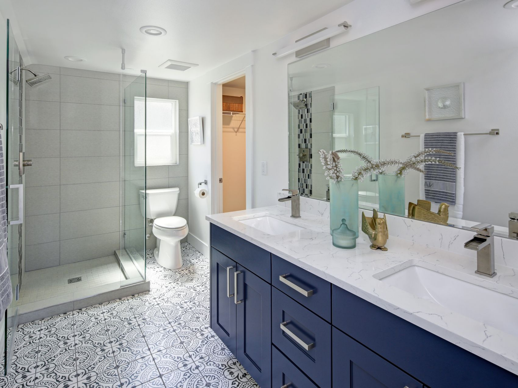 Salle de bains moderne bleue et blanche avec douche en verre, double vasque et sol à motifs.
