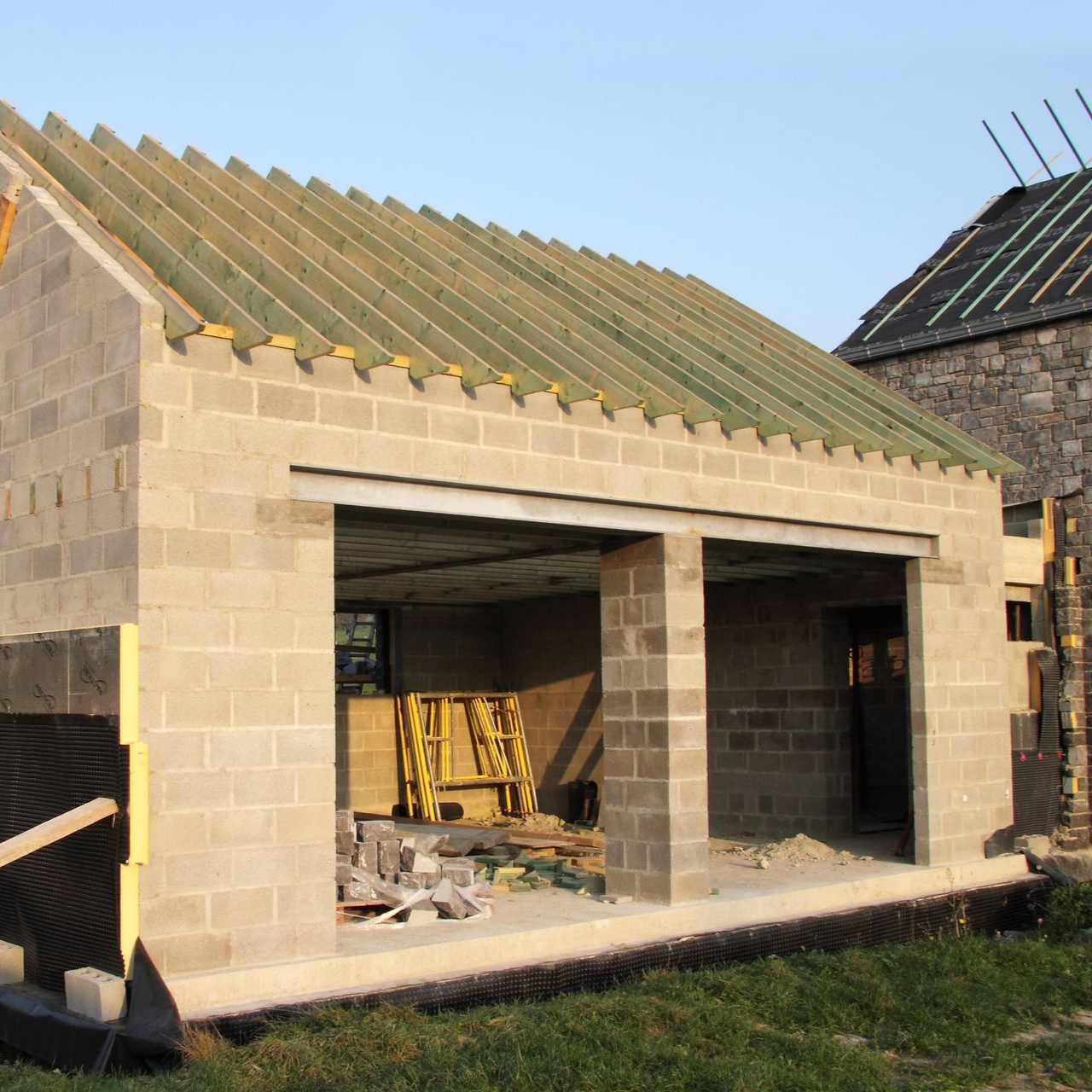 Garage en construction avec murs en parpaings, supports de toiture en bois.