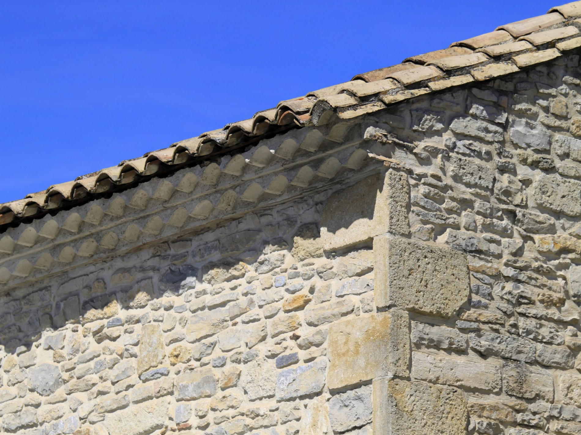 Bâtiment d'angle en pierre avec toit en tuiles contre un ciel bleu.