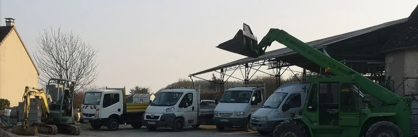 Des engins de chantier sont garés sur un parking près d'un bâtiment. Un chariot élévateur vert est levé.