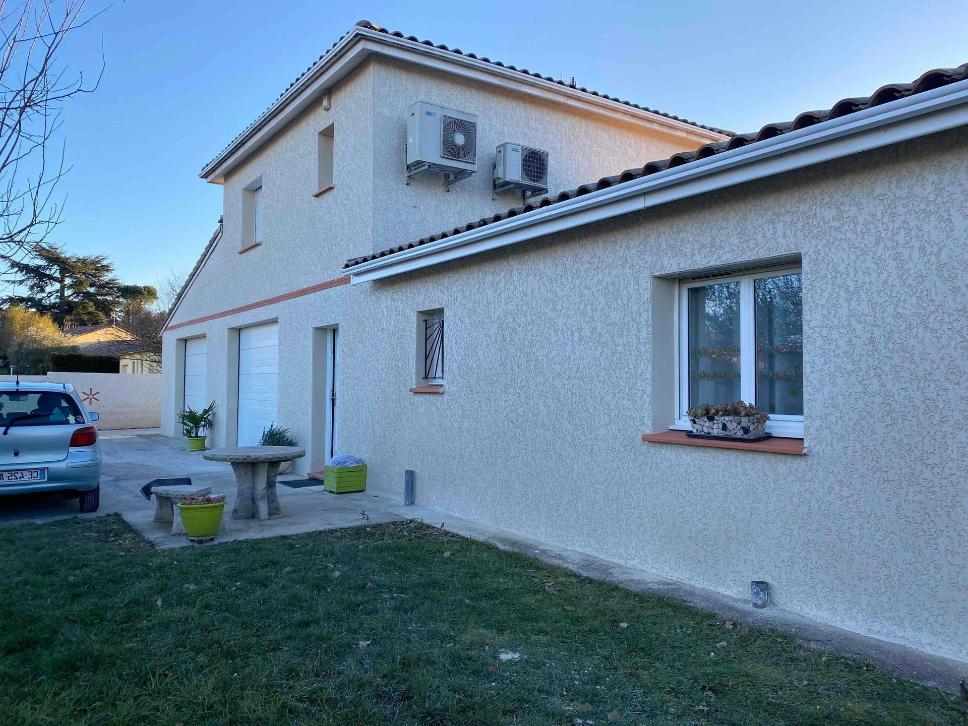 Maison enduite d'un crépi texturé avec un jardin, du mobilier d'extérieur, des plantes en pot et une voiture garée