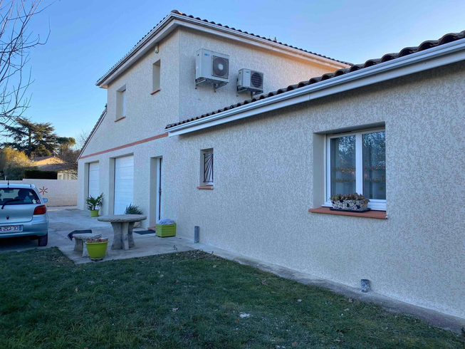 Extérieur d'une maison au crépi texturé de couleur crème avec un jardin gazonné, une table et une voiture garée