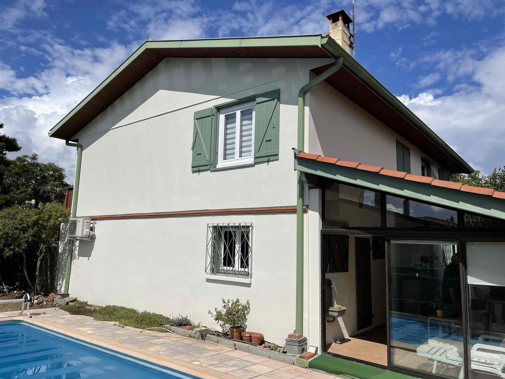 Maison blanche à deux étages avec des volets verts après un ravalement de façade