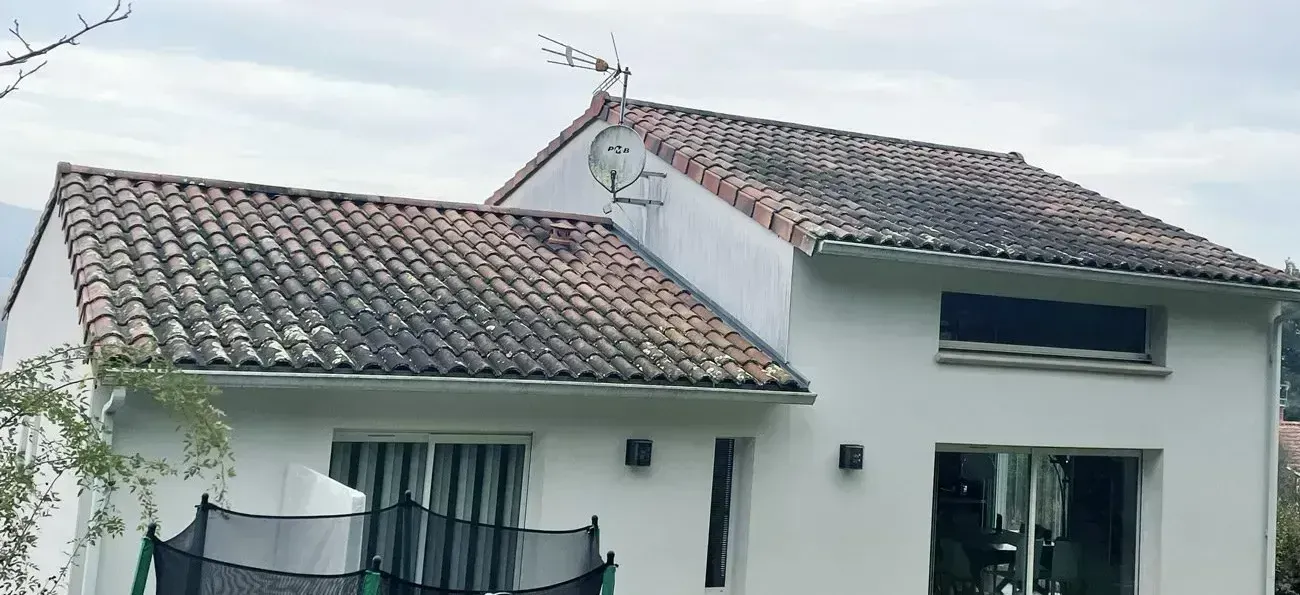 Maison au toit de tuiles sales, petit balcon et grandes fenêtres, avant un démoussage