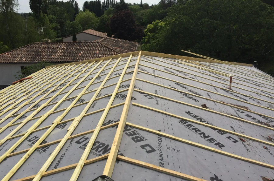 Toiture en construction avec sous-toiture grise et liteaux en bois sur un toit de maison en pente