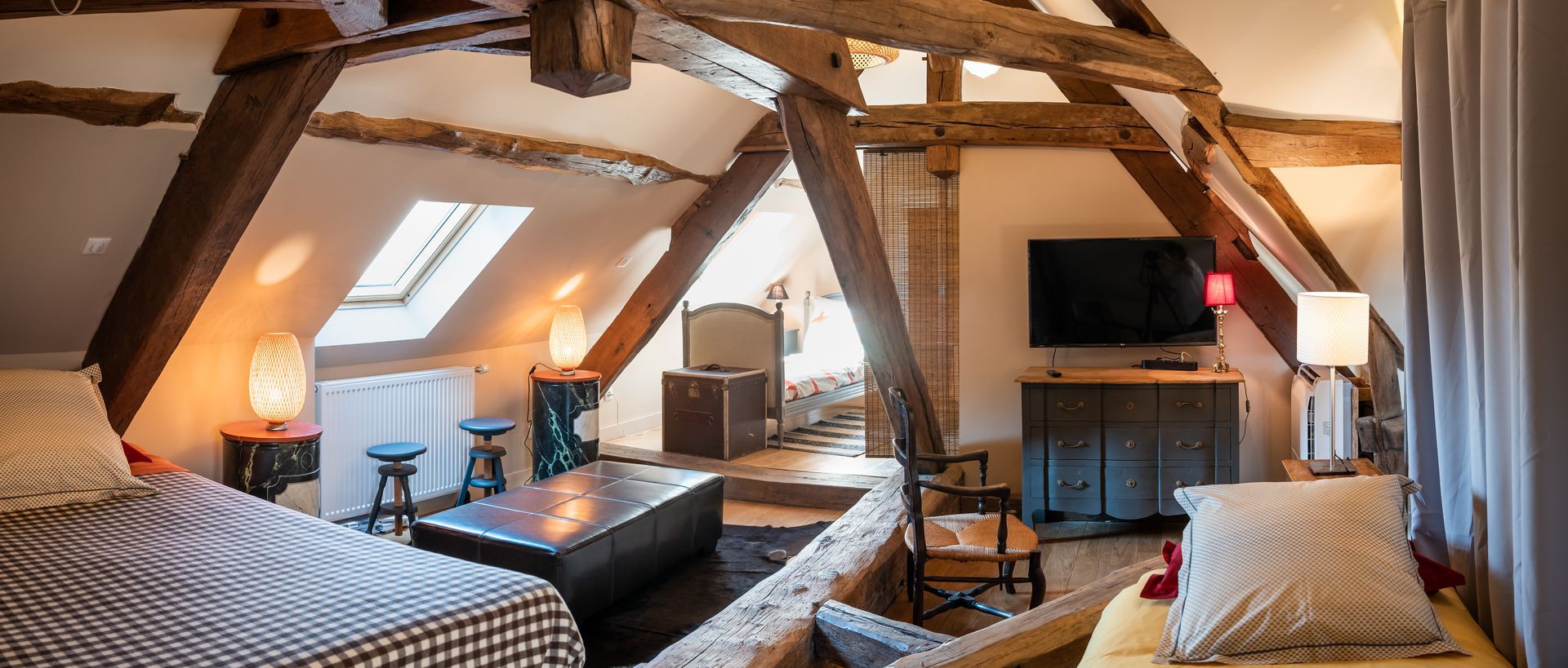 Chambre mansardée avec poutres apparentes, puits de lumière et mobilier