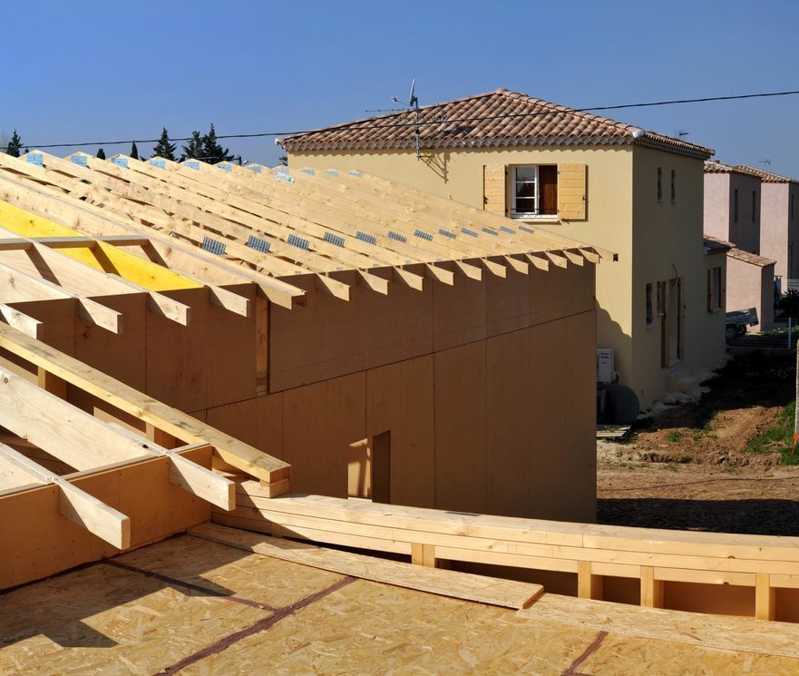 Maison partiellement construite avec charpente apparente et murs beiges sur un chantier ensoleillé