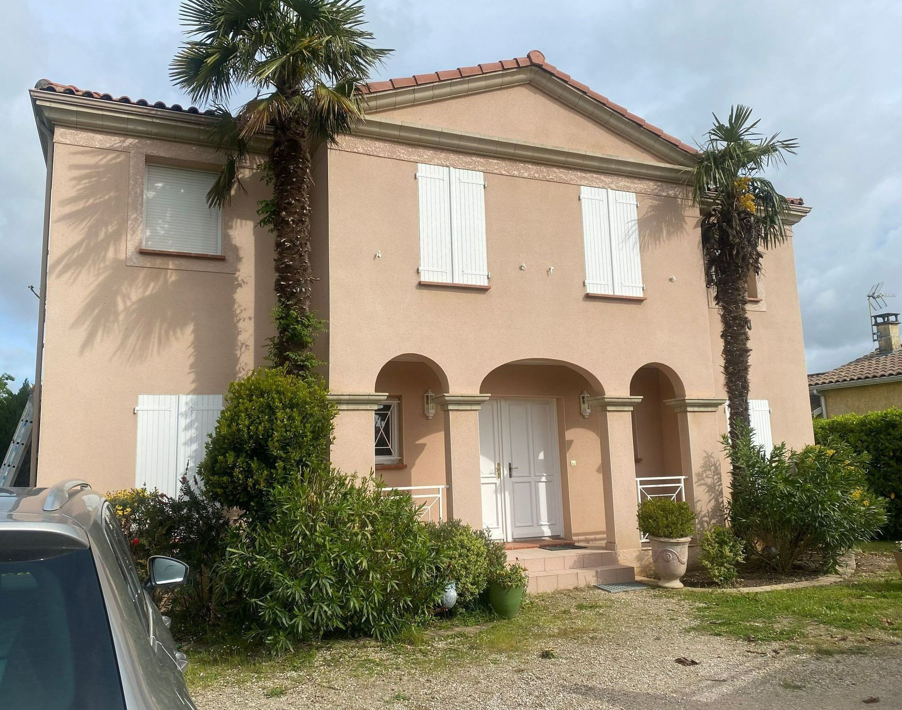 Maison beige à deux étages avec volets blancs, porche voûté et verdure, après un nettoyage de façade